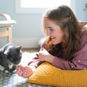 Amanda lying on her stomach smiling while a grey cat noses her fingers